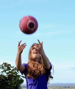 Low angle view of young woman playing with ball against clear sky