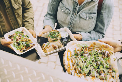 Midsection of customers holding indian street food in city