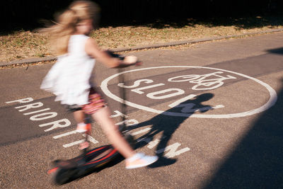 Blurred motion of girl riding push scooter on road