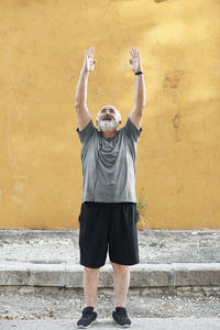 An overweight older man is stretching in front of a wall