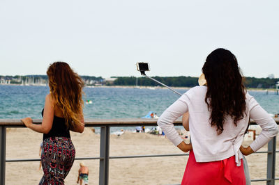 Woman with friends taking selfie by railing at beach
