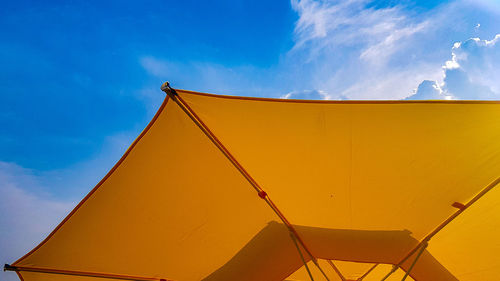 Low angle view of yellow umbrella against blue sky