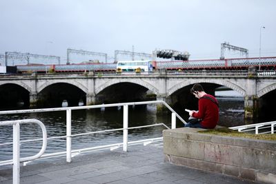 Man standing on bridge over river against sky