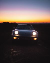 Car on illuminated field against sky at sunset