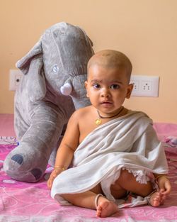 Full length portrait of cute baby girl sitting by toy on bed at home