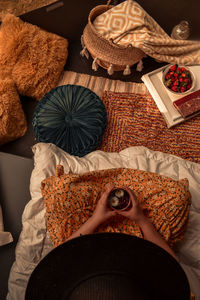 High angle view of woman sitting on mattress with cozy pillows and blankets on the ground, bohemian