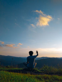 Rear view of man sitting on land against sky during sunset