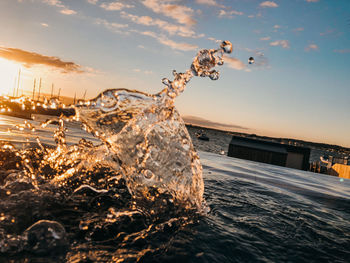 Water splashing in swimming pool against sky during sunset