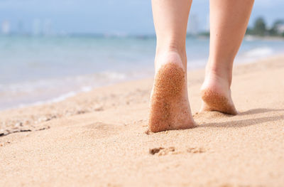 Low section of woman walking on sand at beach