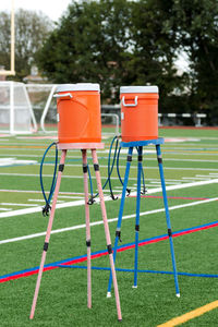 Two water coolers on stands with multiple spouts to hydrate athletes practicing on green turf field.
