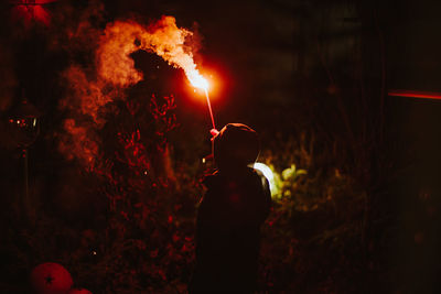 Rear view of man with distress flare emitting smoke at night