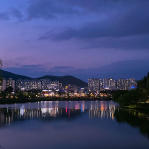 Illuminated buildings by river against sky at night