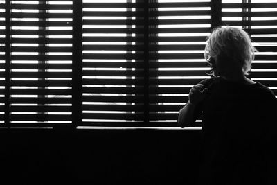 Rear view of boy looking through window at home