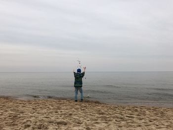 Rear view of man standing on beach against sky