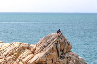 People on rock by sea against clear sky