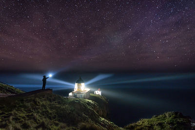 Person holding flashlight while standing on hill against milky way