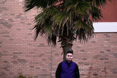 Portrait of boy standing by tree against brick wall