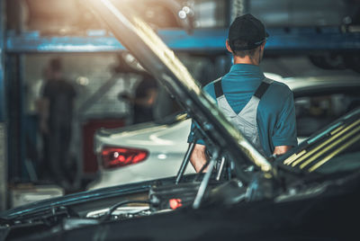 Rear view of mechanic by car in garage