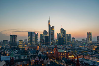 Illuminated cityscape against clear sky during sunset