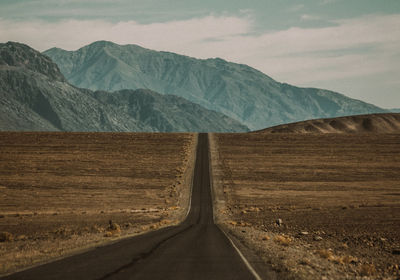 Country road leading towards mountains against sky