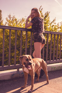 Rear view of young woman with dog standing by railing on footbridge