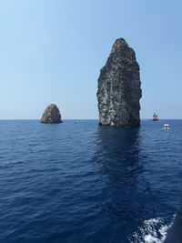 Rock formation in sea against clear blue sky