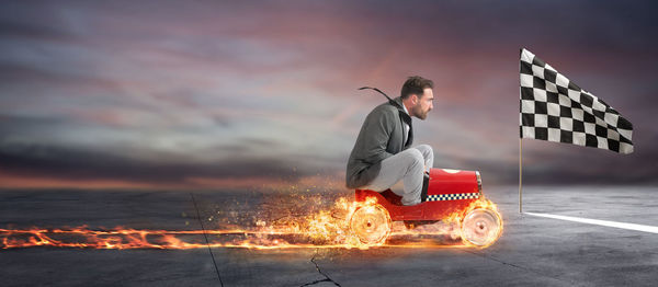 Man sitting on fire against sky at sunset