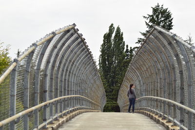 Woman looking away while standing on footbridge against sky