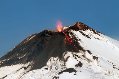 Firework display on snowcapped mountains against clear sky