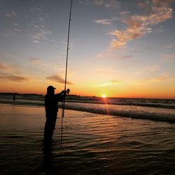 Silhouette man holding fishing rod at beach during sunset