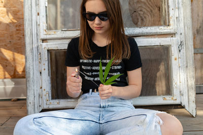 Young woman igniting sparkler while sitting on wood