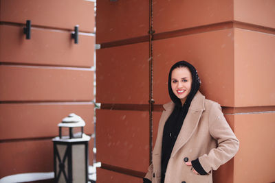 Portrait of smiling young woman standing against wall