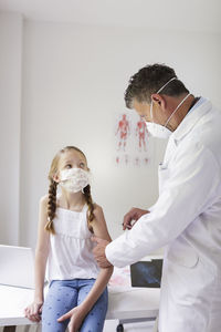 Doctor wearing mask giving injection to girl