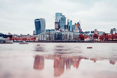 Modern buildings by river against sky in city