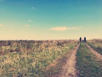 Rear view of family walking on dirt road against blue sky