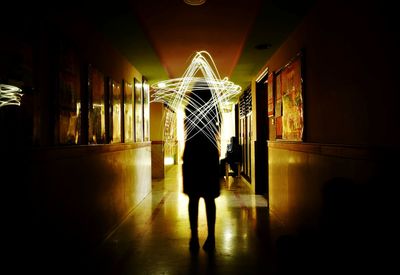 Rear view of man walking in illuminated corridor