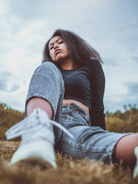 Midsection of woman sitting on field against sky