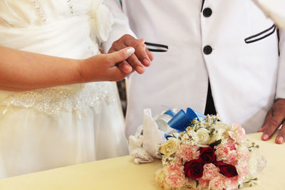 Midsection of wedding couple standing by bouquet on table