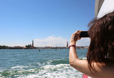 Rear view of woman photographing sea against sky