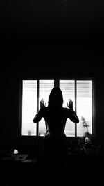 Rear view of silhouette woman standing in window