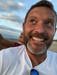 Close-up of thoughtful man smiling against sky during sunset