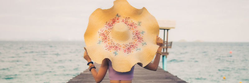  portrait back young asian woman in a purple bra touching a hat on her head on a bridge at the beach