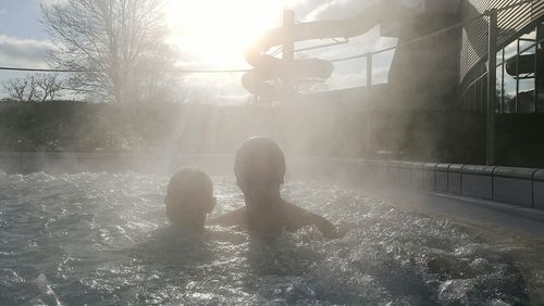 Rear view of boys on water against sky