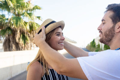 Man putting hat on girlfriend's head while standing in the city