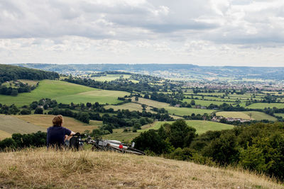 Rear view of man with bicycle sitting on hill