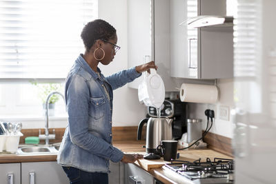 Woman pouring water into kettle in kitchen