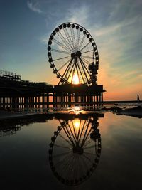 Reflection of ferris wheel in sea against sky during sunset