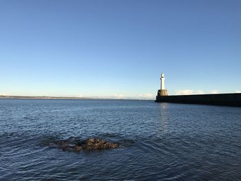 Lighthouse by sea against clear blue sky