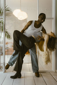 Happy young man dancing with girlfriend near doorway at home