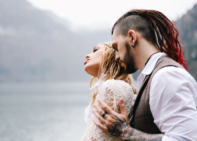 A loving married couple the bride and groom in suits celebrate wedding near the mountains and water